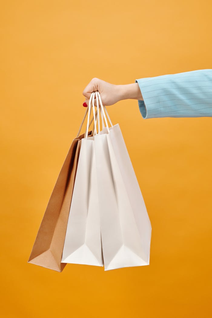 Close-up of a hand holding shopping bags against a bright yellow background, perfect for retail concepts.